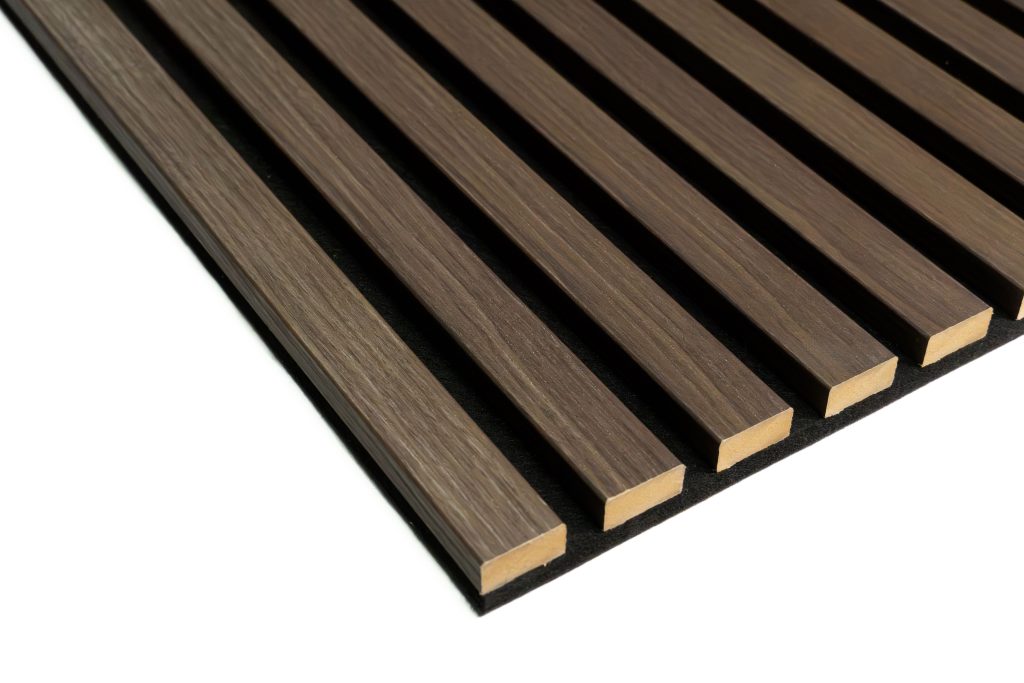 Close-up of WoodUpp slatted acoustic wall panel: evenly spaced, rectangular brown wood-effect slats with subtle grain mounted on a black acoustic backing. The WoodUpp product shows clean edges, alternating gaps for sound absorption, showcasing a walnut-tone finish and modular, ready-to-install cladding.