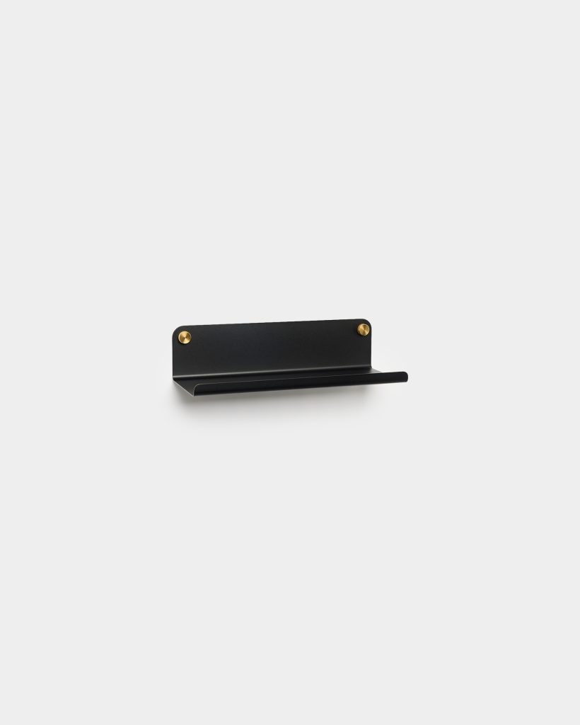 WoodUpp small black wall shelf with a slim horizontal lip and rounded backplate, mounted by two visible brass screws. Minimal matte metal design creates a narrow ledge suitable for keys, phones or mail. Simple modern wall-mounted storage and display from WoodUpp.