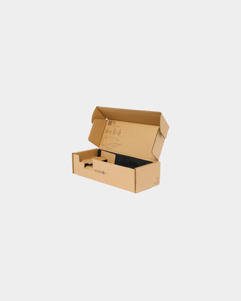 Open WoodUpp cardboard box photographed against a white background, showing a printed assembly diagram on the inner lid, a corrugated cardboard insert compartment, and a black fabric pouch inside. The WoodUpp logo is visible on the front exterior of the box, highlighting branded packaging.