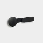 WoodUpp black wall hook mounted on a white wall, featuring a round black-stained oak wooden disc peg paired with a slim matte black metal strap-style hook extending horizontally, offering a minimalist, contemporary coat or towel hook with visible wood grain and seamless low-profile mounting.