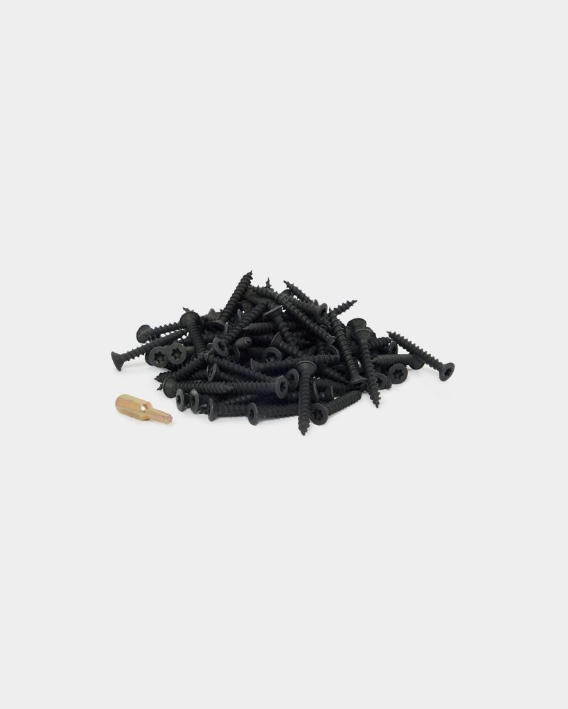WoodUpp product image showing a pile of black, coarse-threaded wood screws with flat, countersunk cross-head heads and self-tapping points, accompanied by a single gold-colored driver bit. The screws are stacked on a white background, highlighting their black corrosion-resistant coating and aggressive threads.