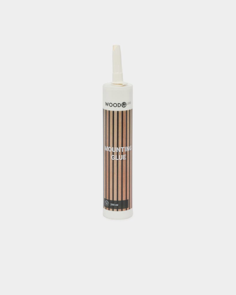 A WoodUpp 290 ml mounting glue cartridge: a tall white cylindrical tube with a pointed applicator nozzle, decorated with vertical wood-grain stripes and bold white "MOUNTING GLUE" lettering; the WoodUpp logo appears near the cap, presented against a plain light background.