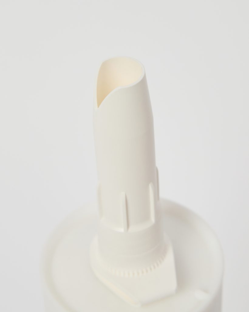 Close-up of a WoodUpp white plastic precision applicator nozzle attached to a cartridge cap, showing the tapered angled spout, ribbed locking collar and round cap base. The image highlights the smooth, off-white plastic finish and detail of the WoodUpp glue nozzle and cap assembly.