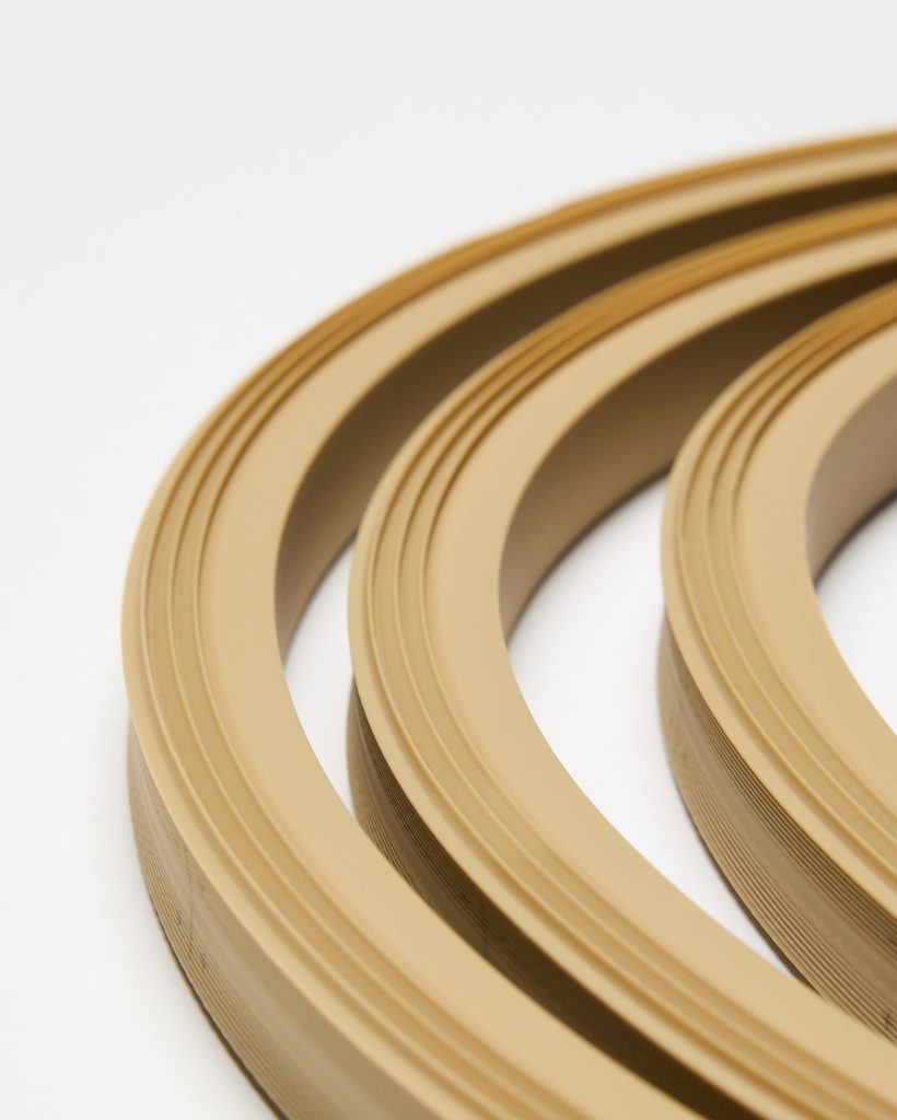 Close-up of three WoodUpp edge banding coils: warm beige, flexible edging rolls with smooth matte faces and subtle concentric grooves along the outer profile. The layered cross-section of the bands is visible, showing thin stacked layers; ideal decorative edging for furniture and cabinetry.