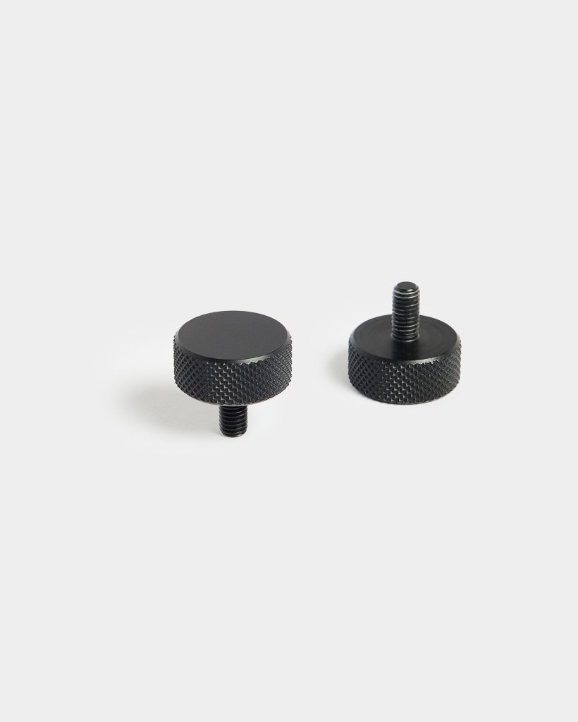 Image shows two WoodUpp black knurled metal thumb screws: compact round heads with diamond-pattern grip and short threaded studs. One screw stands upright displaying its threads, the other lies flat revealing the smooth top. Matte finish and textured sides emphasize their durable hardware design.