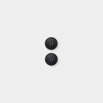 Minimal product shot for WoodUpp showing two matte black circular hardware mounts, each a shallow domed disc with textured central boss and visible central screw, aligned vertically on a clean light-gray background, highlighting their compact, low-profile design and subtle shadowing.