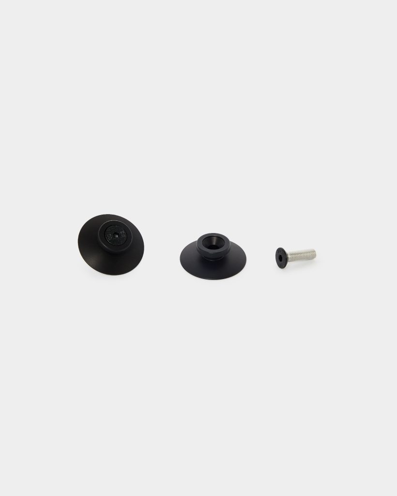 WoodUpp mounting hardware: three items on white background — two matte-black flanged adapter caps (one with a recessed socket, one with a raised collar) and a short silver countersunk screw with black flat head. Clean studio view showing shapes and detail of each component.