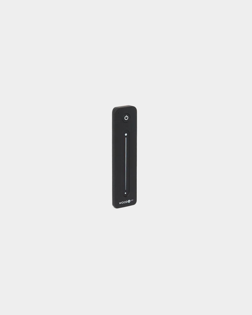 Single WoodUpp black slim remote control standing upright on a pale grey background. Rectangular rounded-edge handset features a circular power button at top, a long illuminated vertical touch slider with indicator dots, and the WoodUpp logo printed at the bottom of the device.