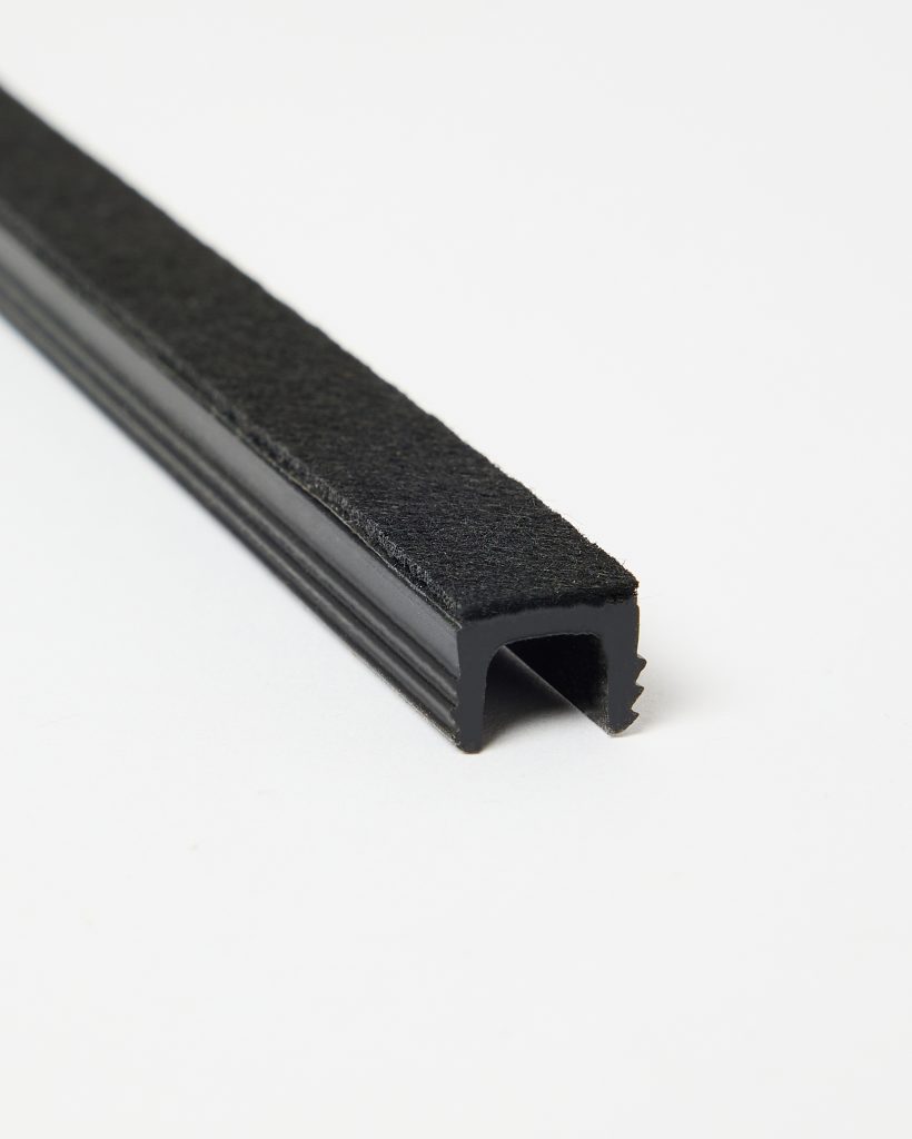 Close-up of a WoodUpp black U-shaped rubber edge trim with an integrated felt strip on its top surface. The profile shows internal serrated jaws for secure clamping and a hollow channel for edge protection, photographed on a white background highlighting texture and detail.