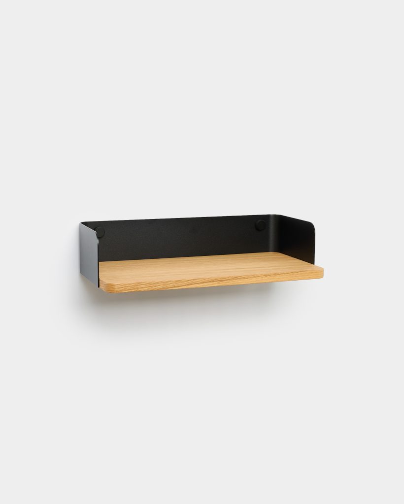 WoodUpp floating wall shelf featuring a light oak wooden board supported by a matte black powder-coated steel surround and backplate. The minimalist shelf shows rounded black metal sides and two visible mounting caps, displayed empty against a plain light-grey wall for a clean, modern look.