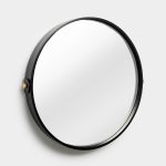 WoodUpp round wall mirror with thin black-stained wooden frame, circular glass face and a single visible brass mounting accent on the left; photographed against a neutral light-gray wall, showing the mirror's minimalist, contemporary design and slim profile, highlighting high-quality craftsmanship.