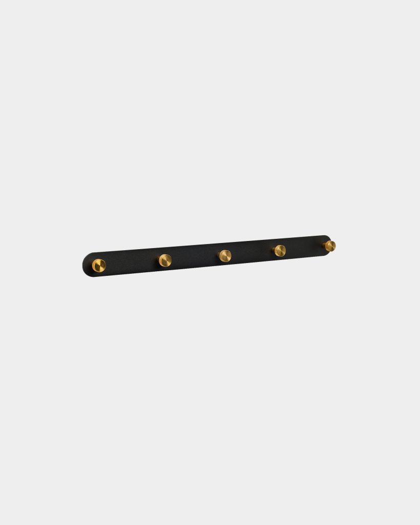 WoodUpp wall-mounted coat rack: a slim matte-black horizontal rail featuring five evenly spaced round brass pegs. Minimal, modern design with cylindrical golden hooks set into a rounded-edge black strip, ideal for hanging coats, bags, or towels while adding a refined contrast to interior walls.