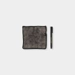 WoodUpp microfiber cloth and repair marker displayed on white background: a square, dark grey plush microfiber cloth with black stitched edges and small circular WoodUpp logo tag, paired with a slim black WoodUpp furniture repair pen with gold branding and removable cap.