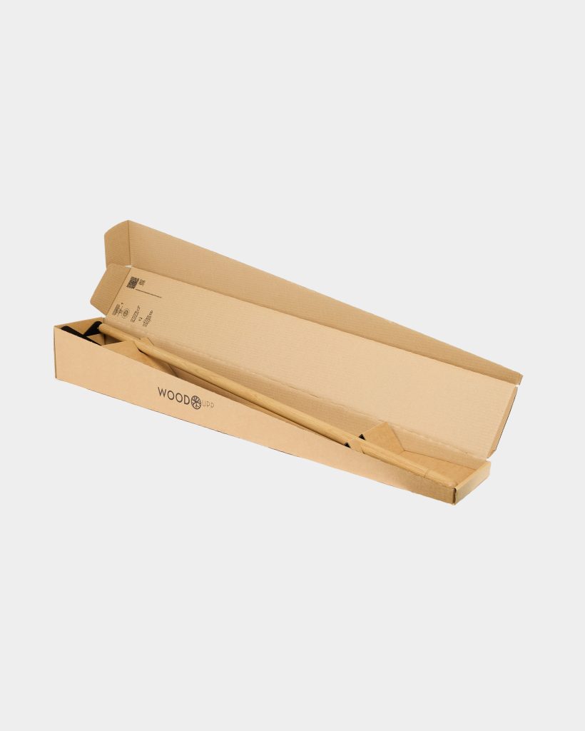 WoodUpp branded long cardboard box opened to reveal a smooth, light wooden pole/handle and shaped wooden supports neatly packed inside. The minimal packaging shows printed assembly icons and the WOODupp logo on the box, highlighting compact, eco-friendly product presentation overall.