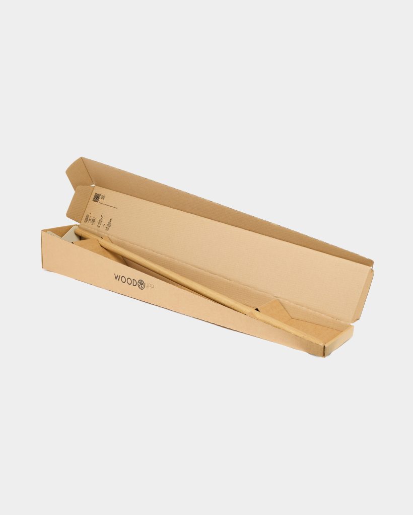 Open recycled cardboard box branded WoodUpp, containing a long smooth light-wood pole and an angled wooden support block nestled inside protective cardboard inserts, photographed on a plain white background to highlight the dowel-like product and accessories for assembly and sustainable packaging details.