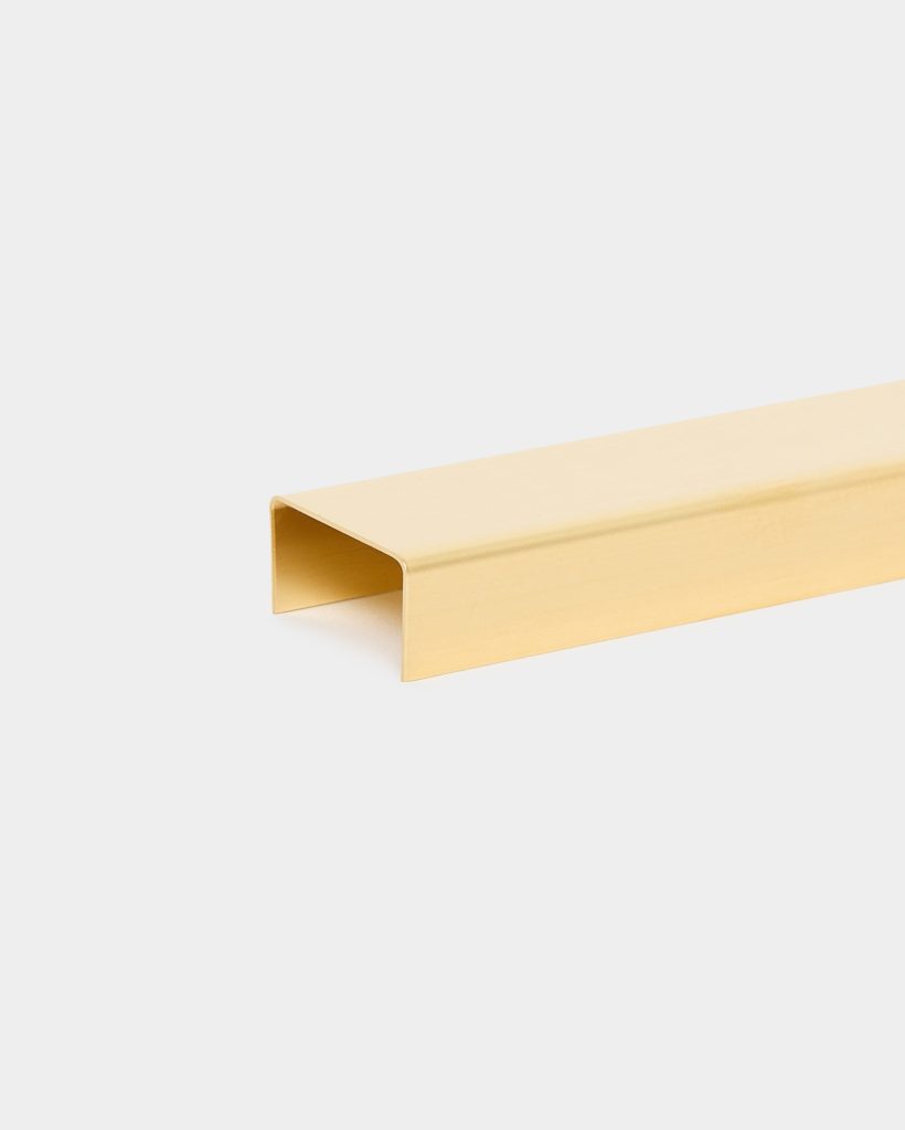 WoodUpp gold U-shaped profile: a single matte brass-finished U-channel trim from WoodUpp shown on a white background. Rectangular hollow profile with rounded inner corners, clean edges and flat top surface, designed for edge protection, cable concealment or decorative architectural trim.