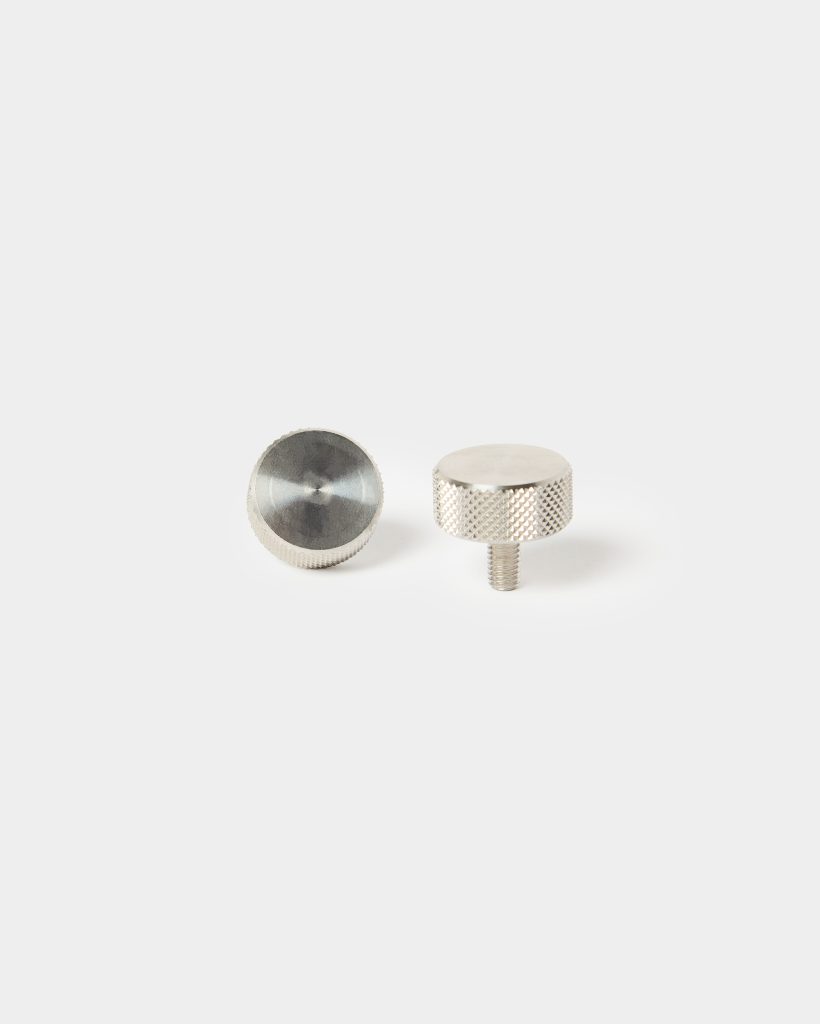 WoodUpp: two small nickel-finished knurled thumbscrews on a white background. One shows the textured cylindrical head and short threaded shaft upright; the other lies flat revealing a smooth circular face. Precision-machined metal finish, diamond knurling for grip, compact hardware for WoodUpp accessories.