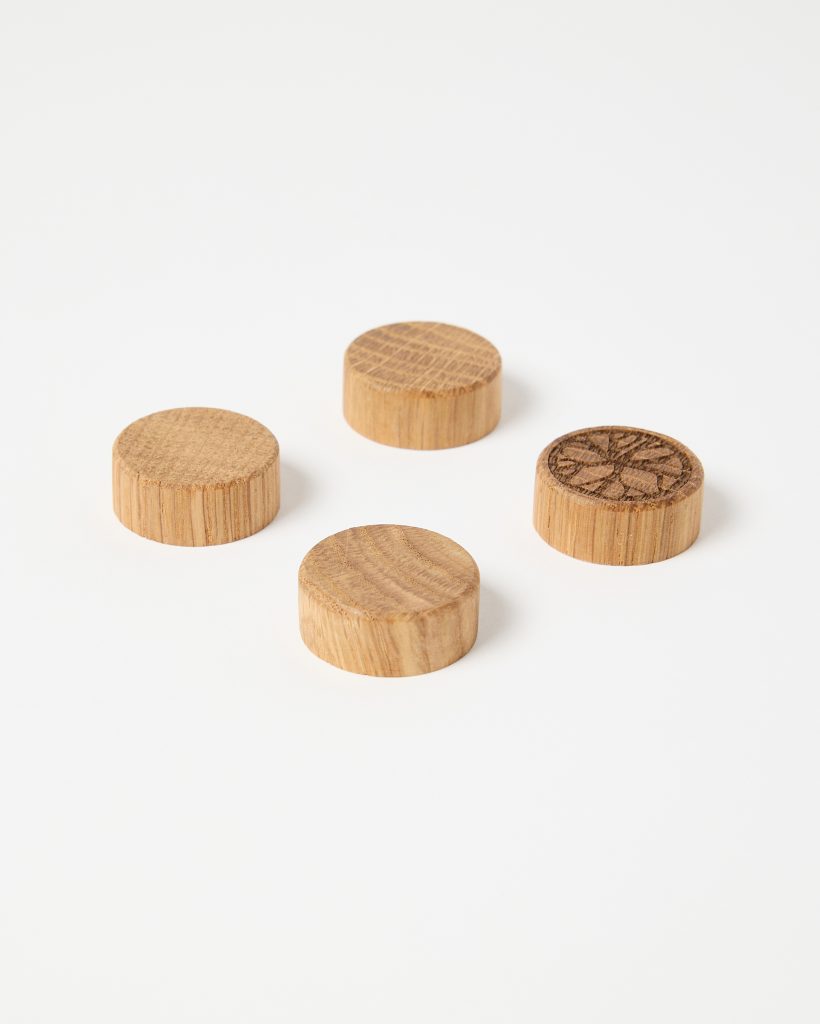 WoodUpp product image of four round oak wooden plugs placed on a white background. Three plugs show smooth, natural grain tops; one plug features a carved decorative starburst motif. Cylindrical edge grain is visible, highlighting WoodUpp’s small wooden furniture caps or screw cover plugs.
