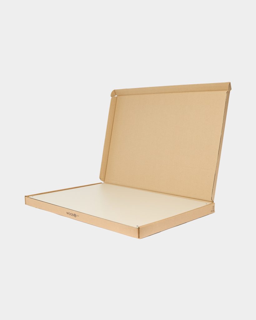 Open WoodUpp corrugated cardboard box with visible WoodUpp logo on the front edge, containing a slim, rectangular white wood panel or board with small protective corner tabs, displayed flat-packed against a plain light background in studio lighting, showing clean edges and minimalist packaging.