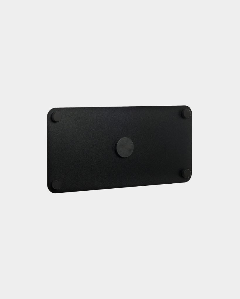 WoodUpp black rectangular mounting plate photographed against a light background, featuring rounded corners, a textured matte finish and five circular rubber pads — one centered and four at each corner — suggesting a slim, minimalist VESA or accessory mounting plate for desks or walls.