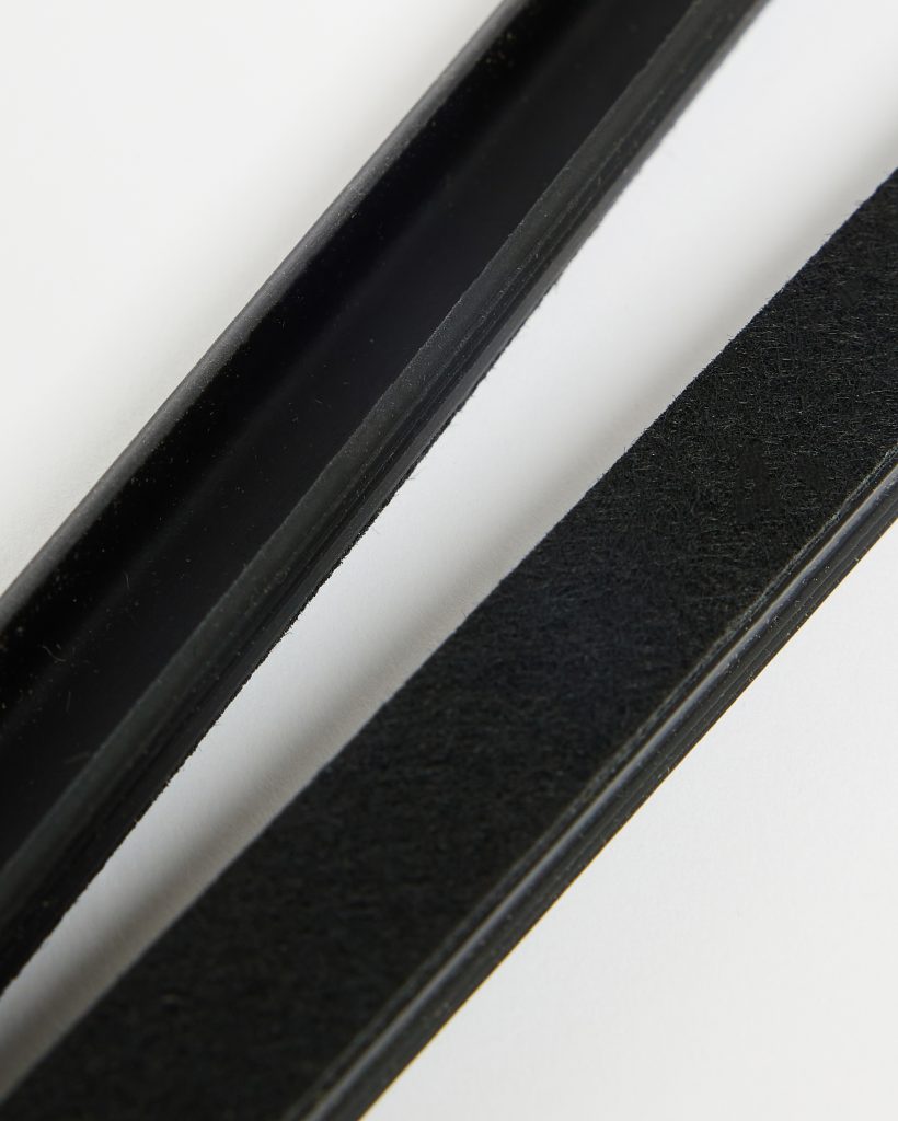 WoodUpp black rubber U‑channel trim and a matching felt‑backed sealing strip lie diagonally on a white background; the rubber profile is a hollow, smooth-edge gasket while the felt strip shows a textured, adhesive-backed surface for cushioning, insulation and gap sealing.