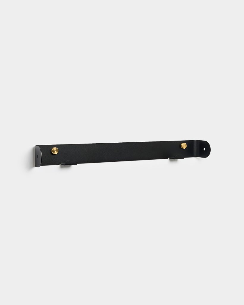 WoodUpp black metal wall rail mounted horizontally on a white background, featuring two round brass pegs and two small integrated black hooks along the slim bar. Minimalist matte finish with concealed screw holes at each end, designed for hanging coats, hats or accessories.
