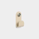 Minimalist WoodUpp single wall hook in matte beige metal, mounted on a white wall. The curved, loop-style hook attaches with a knurled stainless-steel screw head, casting a soft shadow. Clean, modern design suitable for coats, towels, or bags; simple rounded top and rolled front.