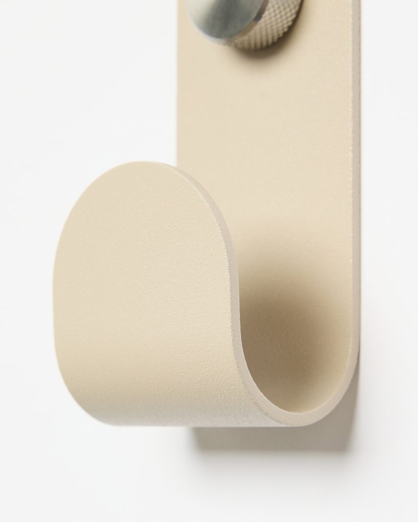 WoodUpp beige powder-coated metal wall hook shown close-up: a single U-shaped curved hook formed from a flat plate, mounted on a vertical backplate with a textured knurled metal screw head visible at top, showcasing a smooth matte finish and rounded, minimal modern design.