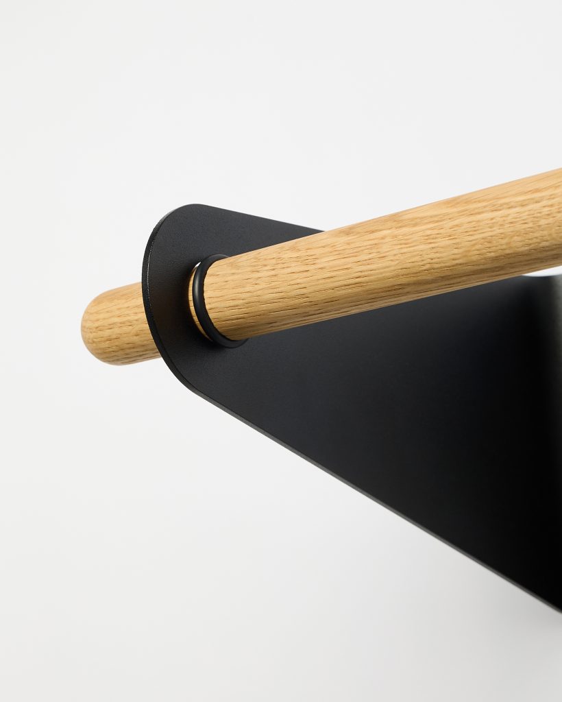 WoodUpp oak rod and matte black bracket close-up showing a light oak dowel seated through a powder-coated steel wall plate. Visible are the rounded dowel end, slim black retaining ring and triangular metal mounting plate, emphasizing minimalist Scandinavian design, visible wood grain and precise low-profile hardware.