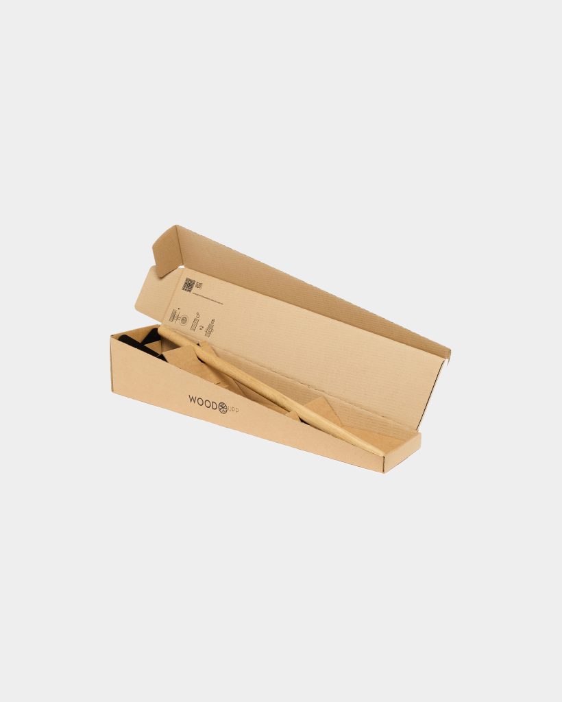 WoodUpp branded cardboard box opened to reveal a long, smooth light-wood handle, a black metal bracket or head piece, and triangular cardboard packaging inserts. The simple kit appears neatly packed for shipping, showing the WoodUpp logo on the box exterior and printed assembly icons inside.