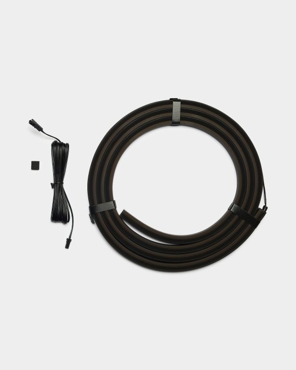 WoodUpp LED floor lighting kit: a large coiled black flexible LED strip, looped and held by two Velcro straps, accompanied by a long black connector cable with plug, a small square adhesive mounting pad, and a short cable tie, shown on a white background.