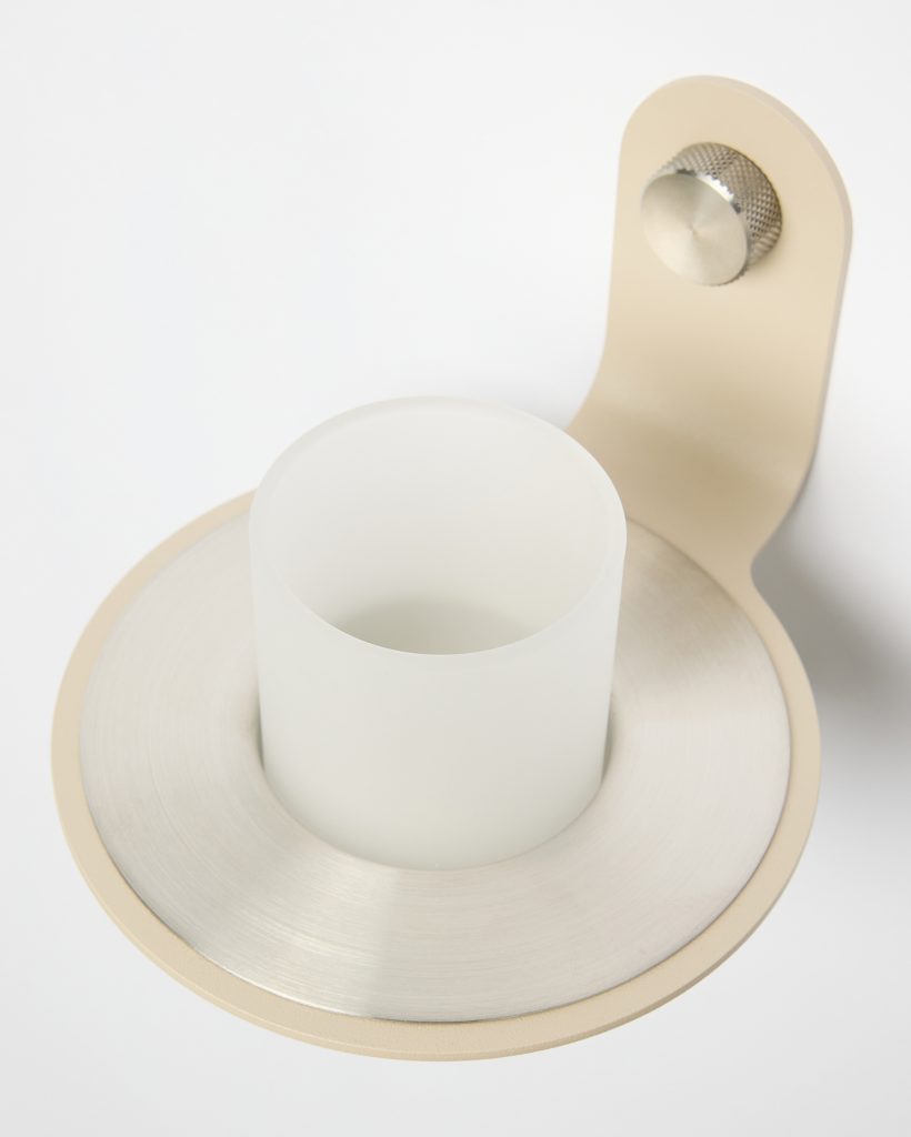 WoodUpp wall-mounted candle holder featuring a matte beige bracket secured with a knurled stainless-steel screw, a circular brushed metal base plate, and a frosted white glass candle cup nested centrally. Minimal, contemporary materials and soft neutral tones emphasize the product’s sleek, functional design.